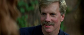 Movie still from “Prince of Darkness” (1987), directed by John Carpenter – A person with a mustache smiling; Close Up shot, Low angle