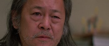 Movie still from “Prince of Darkness” (1987), directed by John Carpenter – An older man with long grey hair and a mustache; Extreme Close Up shot, Over the shoulder angle