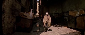 Movie still from “Prince of Darkness” (1987), directed by John Carpenter – A man in a trench coat and hat standing on a street; Wide shot, Low angle