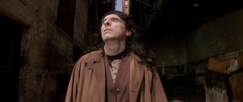 Movie still from “Prince of Darkness” (1987), directed by John Carpenter – A man with long black hair standing in front of a building; Close Up shot, Low angle