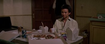 Movie still from “Prince of Darkness” (1987), directed by John Carpenter – A man sitting at a table with a box of pizza; Medium shot, Over the shoulder angle