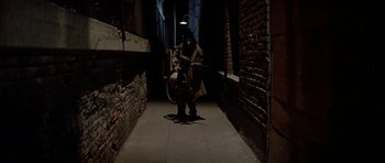 Movie still from “Prince of Darkness” (1987), directed by John Carpenter – A man holding a sword in a dark alleyway; Wide shot, High angle