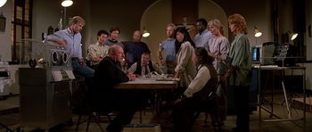 Movie still from “Prince of Darkness” (1987), directed by John Carpenter – A group of people sitting around a table; Wide shot, High angle