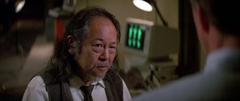 Movie still from “Prince of Darkness” (1987), directed by John Carpenter – An older man with long hair wearing a vest and a tie; Close Up shot, Low angle