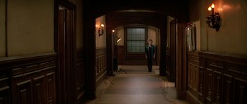 Movie still from “Prince of Darkness” (1987), directed by John Carpenter – A man in a suit and tie standing in a hallway; Wide shot, High angle
