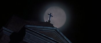 Movie still from “Prince of Darkness” (1987), directed by John Carpenter – A cross on the top of a building in front of a full moon; Extreme Wide shot, Low angle