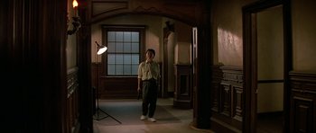 Movie still from “Prince of Darkness” (1987), directed by John Carpenter – A man standing in a dimly - lit room holding a gun; Wide shot, Low angle