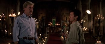 Movie still from “Prince of Darkness” (1987), directed by John Carpenter – Two men are standing next to each other in front of candles; Medium shot, Low angle
