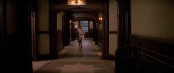 Movie still from “Prince of Darkness” (1987), directed by John Carpenter – A man holding a baseball bat walking down a hall way; Wide shot, High angle