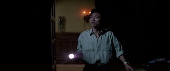 Movie still from “Prince of Darkness” (1987), directed by John Carpenter – A man standing in a dark room holding a flashlight; Medium shot, Low angle