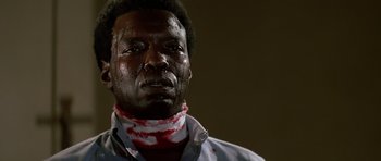 Movie still from “Prince of Darkness” (1987), directed by John Carpenter – A man with a bandage around his neck and face; Close Up shot, Low angle