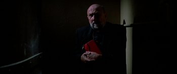Movie still from “Prince of Darkness” (1987), directed by John Carpenter – An older man holding a book in a dark room; Medium shot, Low angle