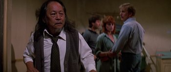 Movie still from “Prince of Darkness” (1987), directed by John Carpenter – A group of people standing in a room; Medium shot, Over the shoulder angle