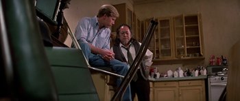 Movie still from “Prince of Darkness” (1987), directed by John Carpenter – Two men are sitting on the stairs in a kitchen; Medium shot, Low angle