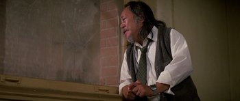 Movie still from “Prince of Darkness” (1987), directed by John Carpenter – An older man with long hair wearing a neck tie; Medium shot, Low angle