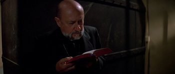 Movie still from “Prince of Darkness” (1987), directed by John Carpenter – An older man reading a book in a dark room; Close Up shot, Low angle