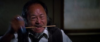 Movie still from “Prince of Darkness” (1987), directed by John Carpenter – An older man with a long beard and a stick in his mouth; Close Up shot, Low angle