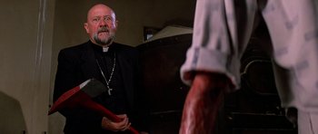 Movie still from “Prince of Darkness” (1987), directed by John Carpenter – A priest holding an axe in front of a man with blood on his hands; Medium shot, Over the shoulder angle