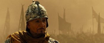 Movie still from “Prince of Persia: The Sands of Time” (2010), directed by Mike Newell – A man wearing a helmet and a scarf is standing in front of a building; Close Up shot, Low angle