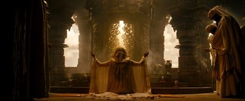 Movie still from “Prince of Persia: The Sands of Time” (2010), directed by Mike Newell – A man in a robe and a cape sitting in front of an altar; Wide shot, Low angle