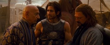 Movie still from “Prince of Persia: The Sands of Time” (2010), directed by Mike Newell – A man in a leather vest is talking to two other men; Medium shot, Over the shoulder angle