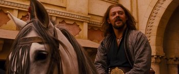 Movie still from “Prince of Persia: The Sands of Time” (2010), directed by Mike Newell – A man with long hair and a beard is sitting on a horse; Medium shot, Over the shoulder angle