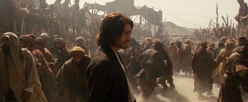 Movie still from “Prince of Persia: The Sands of Time” (2010), directed by Mike Newell – A man with long brown hair is walking through a crowd of people; Medium shot, Over the shoulder angle