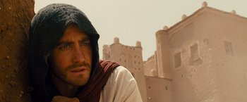 Movie still from “Prince of Persia: The Sands of Time” (2010), directed by Mike Newell – A man in a hooded shirt standing in front of a castle; Close Up shot, Over the shoulder angle
