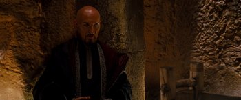 Movie still from “Prince of Persia: The Sands of Time” (2010), directed by Mike Newell – A man with bald head wearing a red and black outfit; Close Up shot, Over the shoulder angle