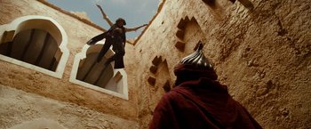 Movie still from “Prince of Persia: The Sands of Time” (2010), directed by Mike Newell – A man in a red robe is standing on a wall; Wide shot, Low angle