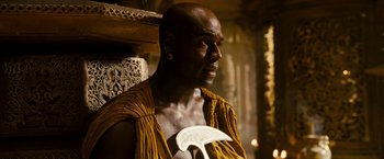 Movie still from “Prince of Persia: The Sands of Time” (2010), directed by Mike Newell – A bald man in a yellow shirt holding a white object; Close Up shot, High angle