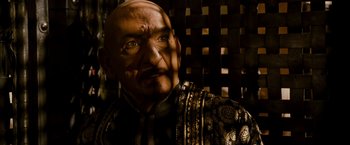 Movie still from “Prince of Persia: The Sands of Time” (2010), directed by Mike Newell – An old man with a bald head wearing a suit and tie; Close Up shot, Over the shoulder angle