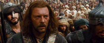 Movie still from “Prince of Persia: The Sands of Time” (2010), directed by Mike Newell – A person with a beard and a crowd of people; Close Up shot, Over the shoulder angle