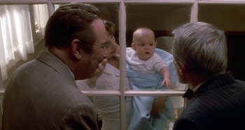 Movie still from “Prizzi's Honor” (1985), directed by John Huston – An older man and a woman looking at a baby through a window; Medium shot, Over the shoulder angle