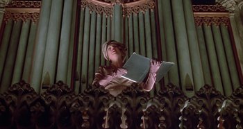 Movie still from “Prizzi's Honor” (1985), directed by John Huston – A woman holding a book in front of a pipe organ; Medium shot, Low angle