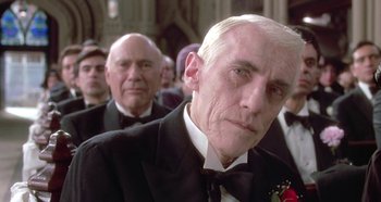Movie still from “Prizzi's Honor” (1985), directed by John Huston – A man in a tuxedo sitting in front of other men; Close Up shot, Low angle