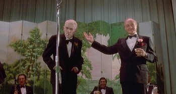 Movie still from “Prizzi's Honor” (1985), directed by John Huston – Two men in tuxedos standing next to each other; Medium shot, Low angle