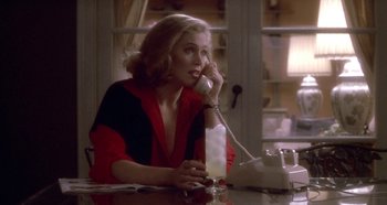 Movie still from “Prizzi's Honor” (1985), directed by John Huston – A woman sitting at a table talking on a phone; Medium shot, Low angle