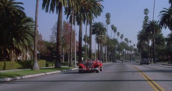 Movie still from “Prizzi's Honor” (1985), directed by John Huston – A couple of cars driving down a street next to palm trees; Extreme Wide shot, Low angle