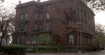 Movie still from “Prizzi's Honor” (1985), directed by John Huston – A large brick building with a bench in front of it; Extreme Wide shot, Low angle