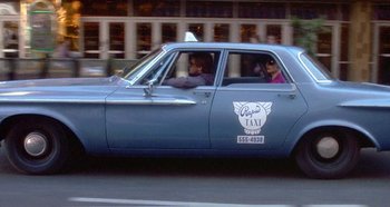 Movie still from “Prizzi's Honor” (1985), directed by John Huston – Two people in a blue car driving down a street; Wide shot, Low angle