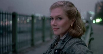 Movie still from “Prizzi's Honor” (1985), directed by John Huston – A woman in a gray jacket standing in front of a fence; Close Up shot, Over the shoulder angle