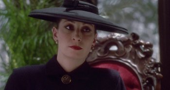 Movie still from “Prizzi's Honor” (1985), directed by John Huston – A woman wearing a black hat sitting in a chair; Close Up shot, Low angle