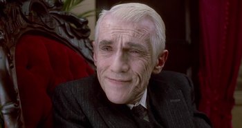 Movie still from “Prizzi's Honor” (1985), directed by John Huston – An older man in a suit and tie smiling for the camera; Close Up shot, High angle