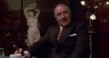 Movie still from “Prizzi's Honor” (1985), directed by John Huston – An older man sitting in front of a statue; Medium shot, Over the shoulder angle