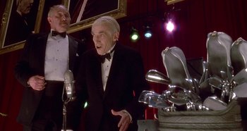 Movie still from “Prizzi's Honor” (1985), directed by John Huston – Two men in tuxedos are standing in front of microphones; Medium shot, Low angle