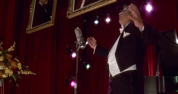 Movie still from “Prizzi's Honor” (1985), directed by John Huston – A man in a tuxedo is singing into a microphone; Medium shot, Low angle