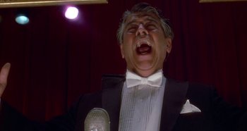 Movie still from “Prizzi's Honor” (1985), directed by John Huston – A man in a tuxedo is singing into a microphone; Close Up shot, Low angle