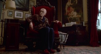Movie still from “Prizzi's Honor” (1985), directed by John Huston – An old man sitting in a chair in front of a painting; Wide shot, Low angle