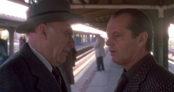 Movie still from “Prizzi's Honor” (1985), directed by John Huston – Two men are standing in a train station talking; Close Up shot, Over the shoulder angle